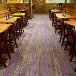 Main dining area at Mother Bear's Pizza with vibrant, multicolored carpet, warm lighting, and wooden tables